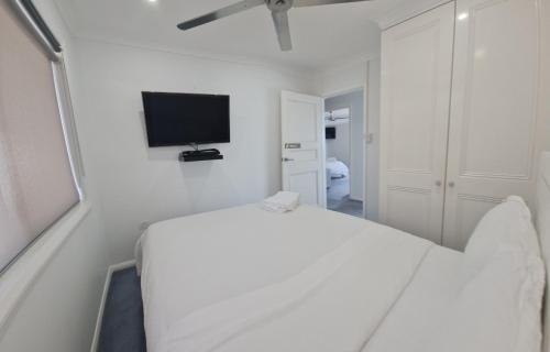 a white bedroom with a bed and a flat screen tv at Bundeena Waterfront Pavilion in Bundeena