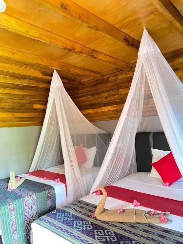 two beds in a room with wooden ceilings at Mirna Homestay in Gili Islands