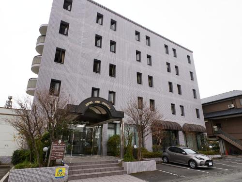a large white building with a car parked in a parking lot at Tabist Hotel New Central in Fuji