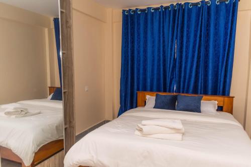 a bedroom with two beds with blue curtains at Arabella Apartments in Bungoma