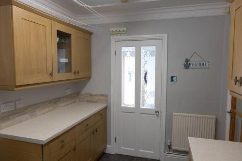 cocina con paredes blancas, armarios de madera y puerta en Spacious bungalow with estuary views, en Carmarthen