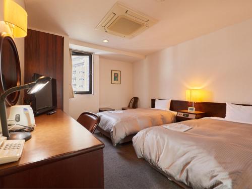 a hotel room with two beds and a desk with a computer at Tabist Hotel New Central in Fuji