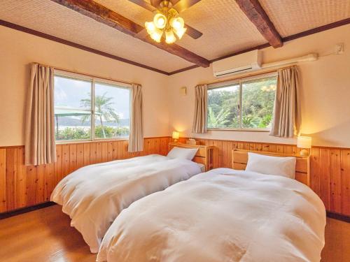 two beds in a bedroom with two windows at Villa AdanRose Amami in Akagina
