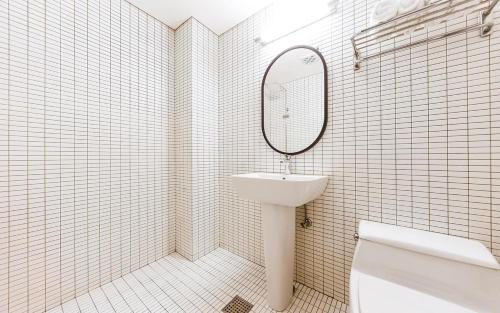 La salle de bains est pourvue de carrelage blanc, d'un lavabo et d'un miroir. dans l'établissement Soho Hotel Airport, à Daegu