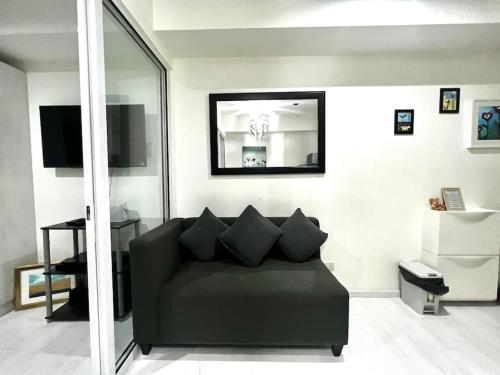 uma sala de estar com um sofá preto e um espelho em Tropez 1br City Light View em Manila