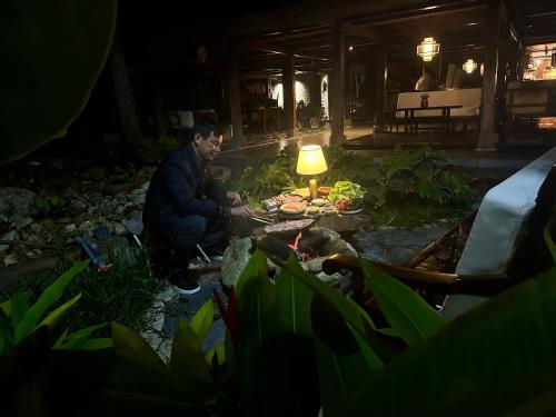 un uomo seduto in un giardino di notte con una lampada di Thavill Retreat HaGiang a Ha Giang