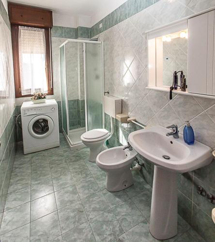 a bathroom with a sink and a toilet and a washing machine at Seaside serenity flat with outdoor pool in Rosolina Mare