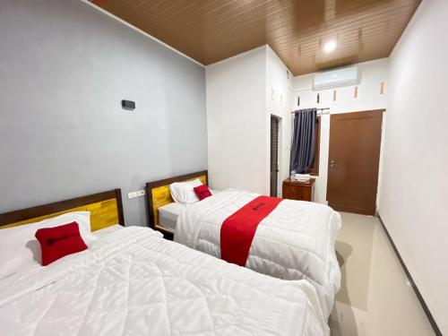 2 bedden in een kamer met witte muren en rode kussens bij RedDoorz at Rose House Simpang Pemda Medan Selayan in Sunggal