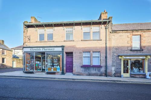 a brick building with a purple door on a street at Arlington House Hotel - Self Check-In Suites in Wooler