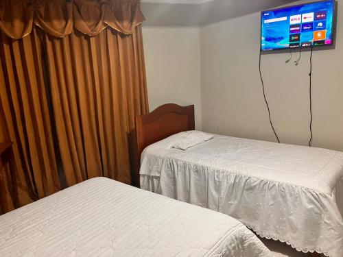 a bedroom with two beds and a tv on the wall at Hostal El Rancho in Huancayo