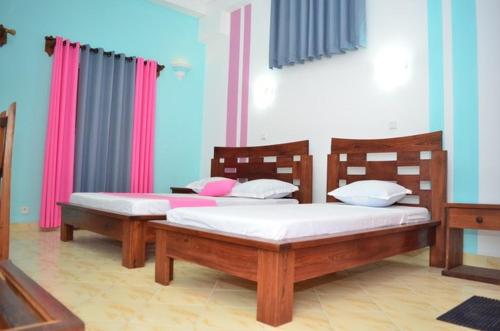 two beds in a room with pink and blue walls at HOTEL AKBAR in Mahajanga