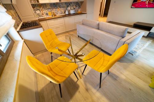 a living room with yellow chairs and a glass table at First Apartments in Focşani