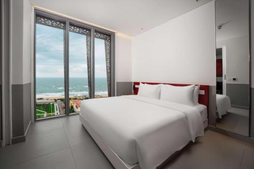 Schlafzimmer mit einem großen weißen Bett und großen Fenstern in der Unterkunft Wink Hotel Tuy Hoa Beach - 24hrs stay & Rooftop Pool Bar in Tuy Hoa