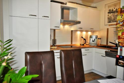 a kitchen with white cabinets and two brown chairs at Möwennest am Twedter Holz in Flensburg