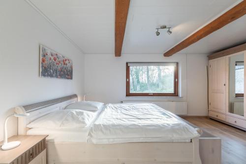 a white bedroom with a bed and a window at De Maade in Enge-Sande