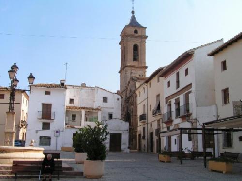 a woman sitting on a bench in a street with a church at EL RINCÓN deMANUELA in Requena