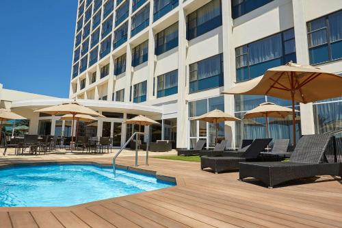 a pool with chairs and umbrellas next to a building at Garden Court Kings Beach in Port Elizabeth