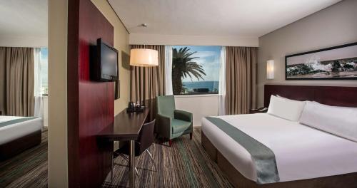 una camera d'albergo con letto, scrivania e finestra di Garden Court Kings Beach a Port Elizabeth