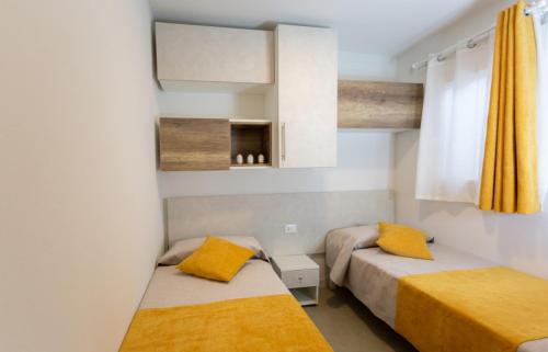 two beds in a small room with yellow pillows at Village Camping Joker in Cavallino-Treporti