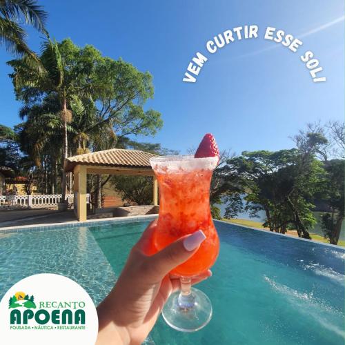 a hand holding a drink in front of a pool at Recanto Apoena in Santa Isabel