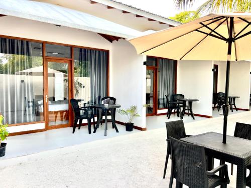 eine Terrasse mit Tischen, Stühlen und einem Sonnenschirm in der Unterkunft Vilu Residence in Maamigili