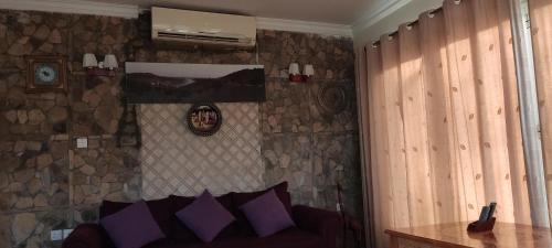 Habitación con pared de piedra, sofá y almohadas moradas. en Hostel Dar Alslam, en Nizwa