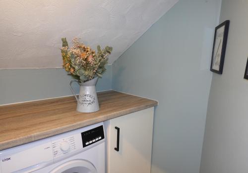 a vase of flowers sitting on a counter next to a washing machine at Mossend Apartment by Klass Living Bellshill in Mossend