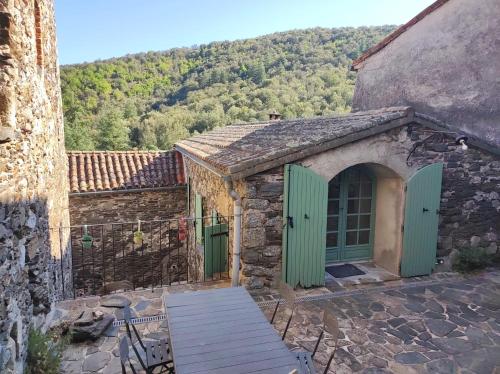 a stone building with green doors with a mountain in the background at Les Deux Voutes de Camias - Gite en Cévennes in Saint-André-de-Majencoules