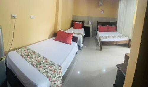 three beds in a room with red pillows at Aunty Arenal Lodge in Fortuna