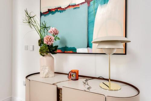 einen Tisch mit einer Lampe und eine Vase mit Blumen darauf in der Unterkunft Tranquil 4-Bed Oasis Modern Chic House in Oxford