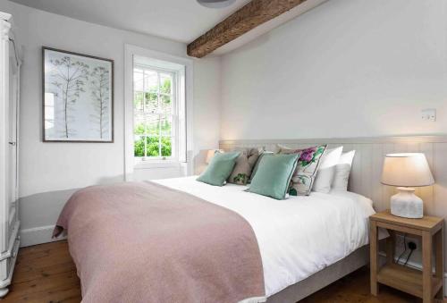 a white bedroom with a large bed with green pillows at Beautiful Cotswold Cottage in Rodborough Stroud in Stroud