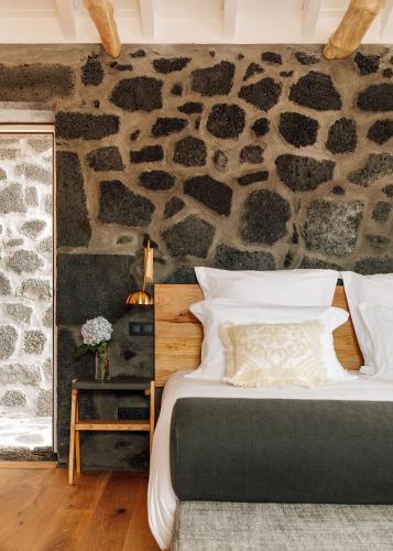 a bed in a room with a stone wall at Adega do Fogo in São Roque do Pico