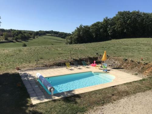 una piscina en un campo con 2 sillas y una sombrilla en Le Bournissard à Cuzance, en Cuzance