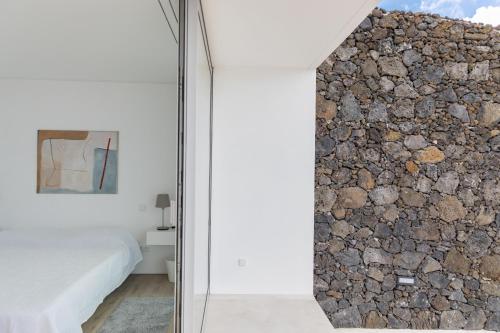Cette chambre est dotée d'un mur en pierre à côté d'un lit. dans l'établissement Casa Neptuno-Lagoa São Miguel, à Lagoa
