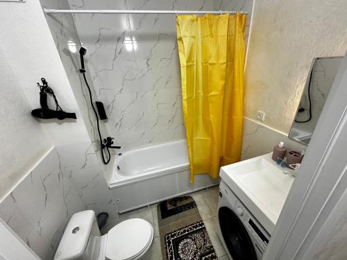 a bathroom with a toilet and a yellow shower curtain at «Созвездие Auezov City: Уютные апартаменты в Сердце города» in Almaty