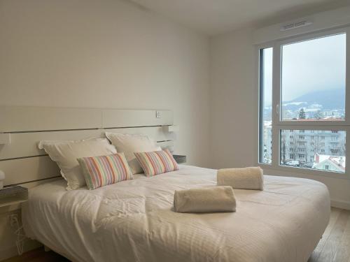 un lit blanc avec deux oreillers et une grande fenêtre dans l'établissement le Bel Alpin, à Annecy