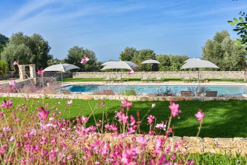 a pool with umbrellas in a garden with pink flowers at Masseria Morrone in Ostuni