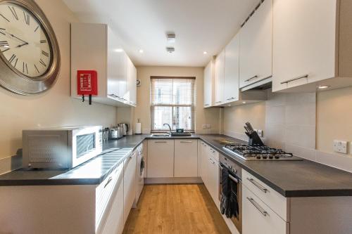 una cocina con armarios blancos y un reloj en la pared en Camstay Abbey Street en Cambridge