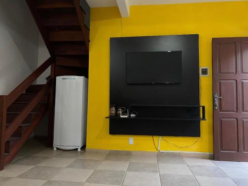 a yellow wall with a flat screen tv and a refrigerator at Casa 300 m Praia Jabaquara in Paraty