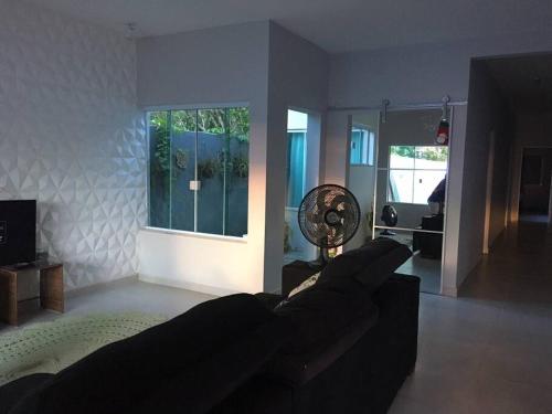 a living room with a black couch and a fan at Casa de Praia in Cananéia