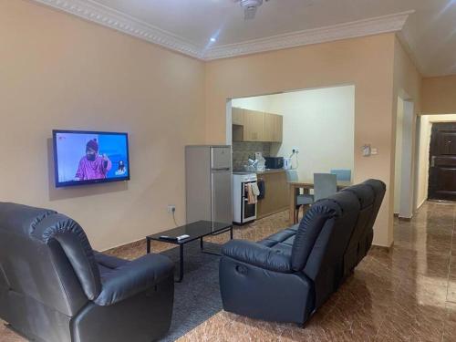 sala de estar con 2 sofás y TV en la pared en Izzy Guest House en Brikama