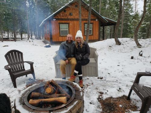 Ein Mann und eine Frau sitzen neben einem Feuer vor einer Hütte in der Unterkunft Whispering Pines cabins in Lakeside