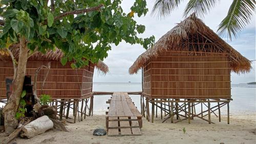 a group of huts on a beach with the ocean at Coco Huts Guest House in Waisai