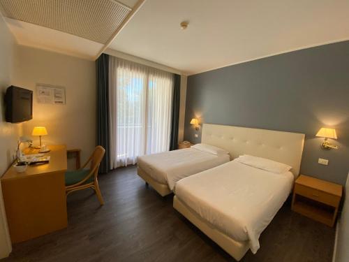 a hotel room with two beds and a desk at Hotel Ristorante Primavera in Godega di SantʼUrbano