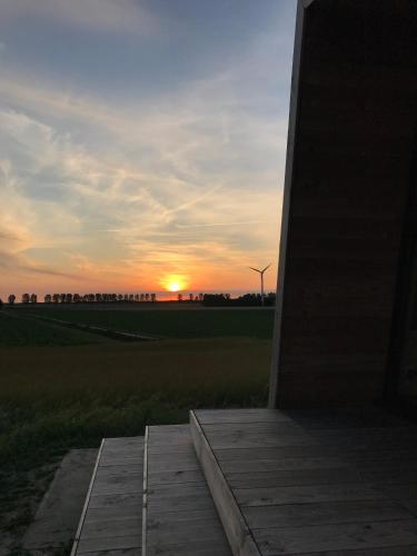 a sunset over a field with a wooden boardwalk at Slapen op de Dijk - Tiny House in Kraggenburg