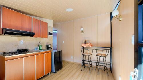 a kitchen with wooden cabinets and two bar stools at Cabañas los Sauces in Tota