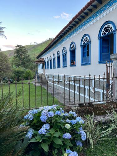 a house with blue windows and a fence and flowers at Fazenda Penedo in Duas Barras