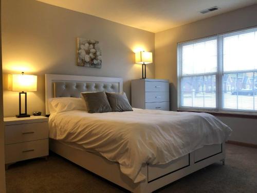 a bedroom with a white bed with two lamps and windows at 2 bedroom apartment RivianISU in Bloomington