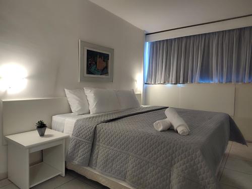 a white bedroom with a bed with a night stand at Hotel Oscar Gold Savassi in Belo Horizonte