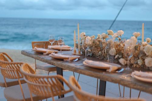 a table on the beach with wine glasses and flowers at Guaycura Boutique Hotel, Beach Club & Spa in Todos Santos